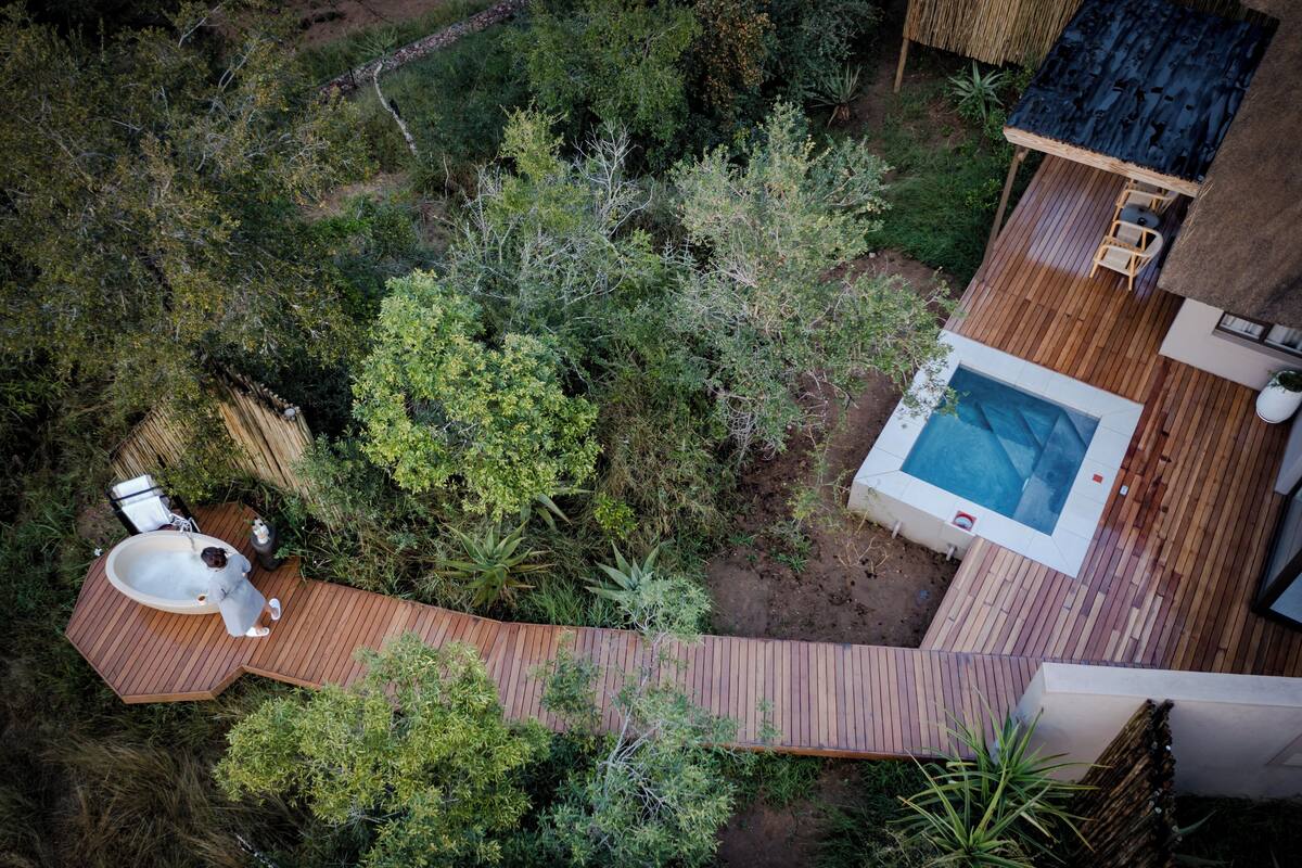An aerial view of a property with a hot tub, wooden deck, and surrounding greenery.