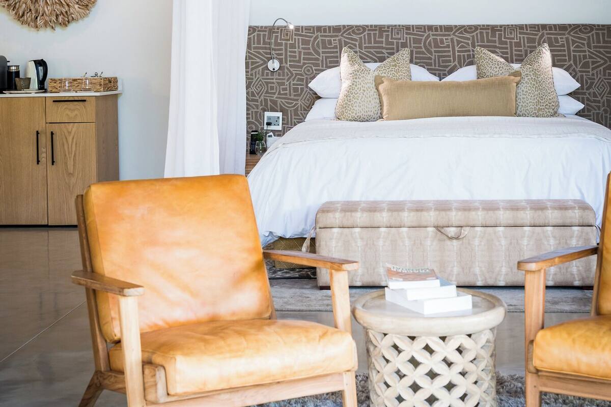 A bedroom with a bed, two chairs, a small round table, a wardrobe, and a decorative wall piece.