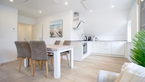 Una cocina moderna con armarios blancos, un comedor con mesa y sillas, y un gran ventanal que proporciona luz natural.