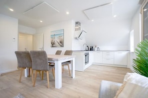 Una cocina moderna con armarios blancos, un comedor con mesa y sillas, y un gran ventanal que proporciona luz natural.