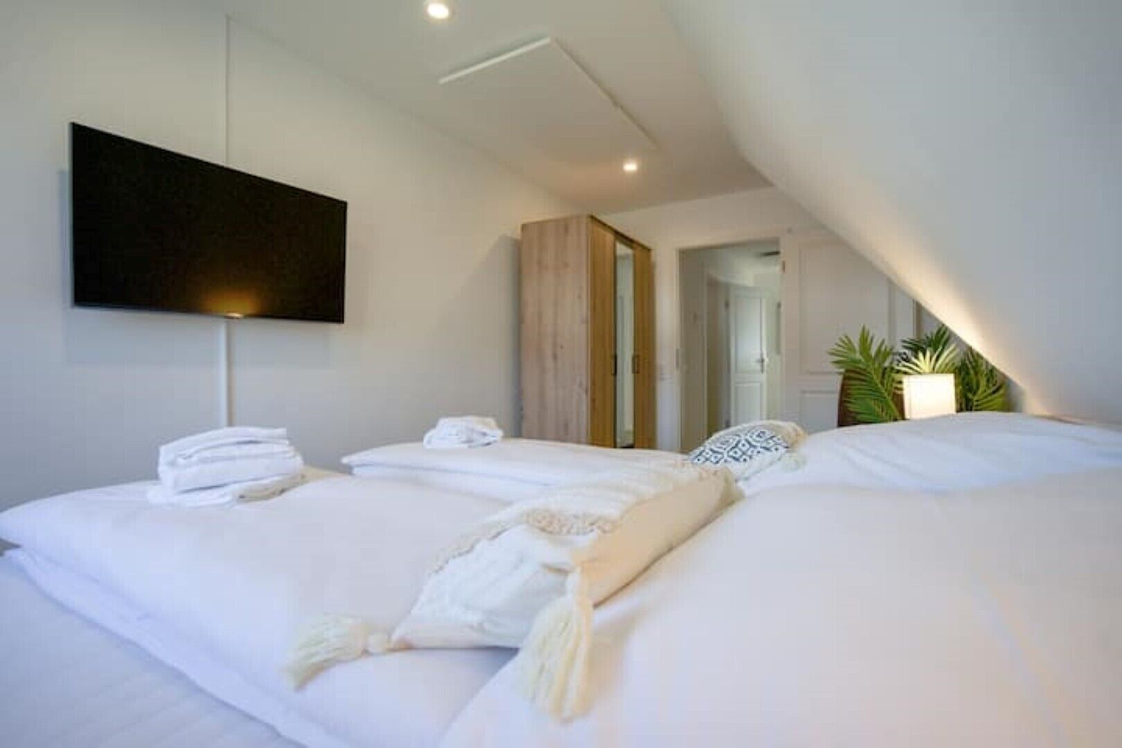 Una habitación de hotel moderna con una cama grande, un televisor de pantalla plana en la pared y una pequeña zona de estar con una silla y una mesa.