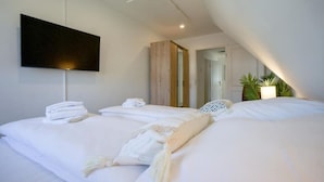 Una habitación de hotel moderna con una cama grande, un televisor de pantalla plana en la pared y una pequeña zona de estar con una silla y una mesa.