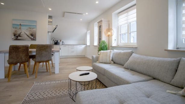 Una sala moderna con sofá, una mesa de comedor con sillas, una zona de cocina y un ventanal grande.