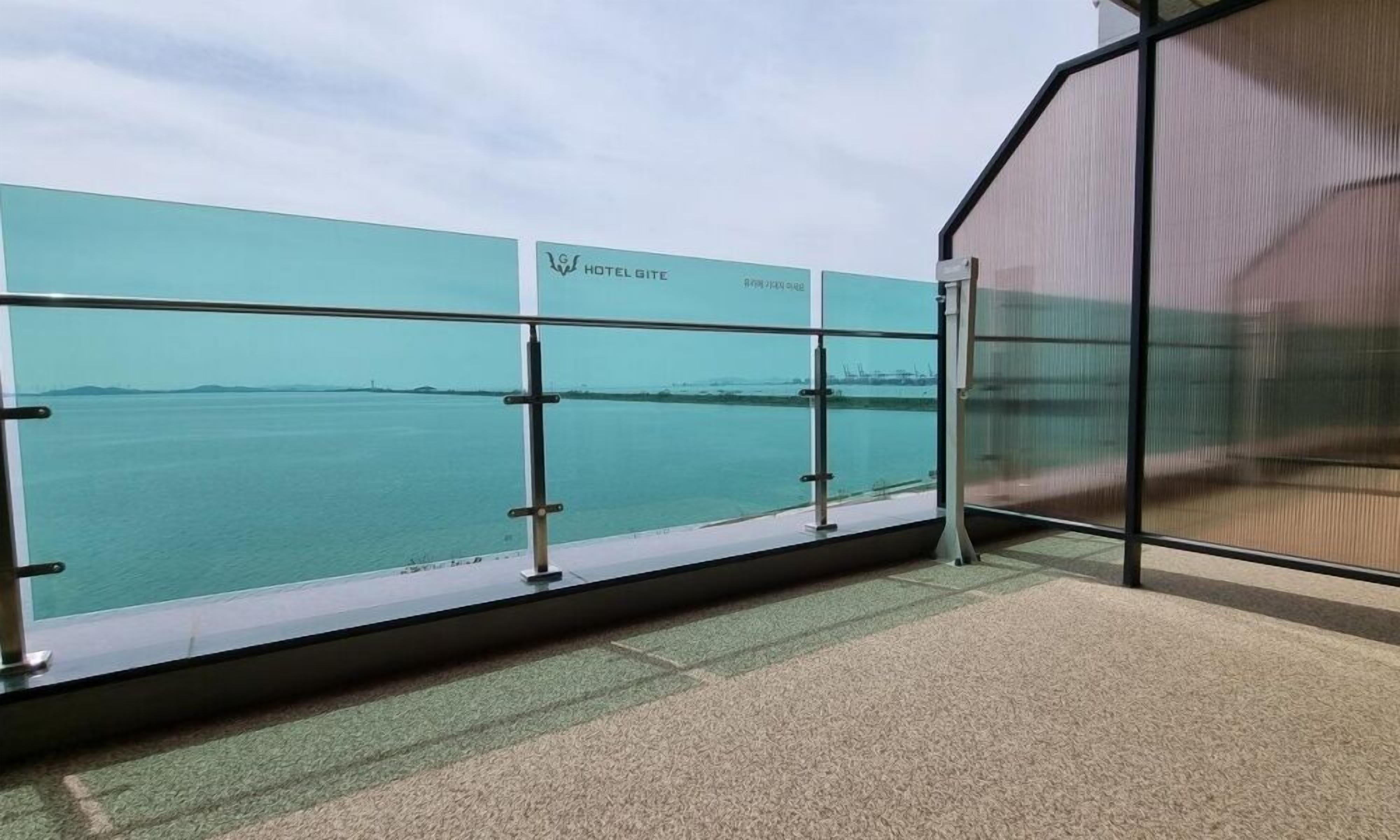 Un balcon avec vue sur la mer, une paroi en verre et une enseigne indiquant « HÔTEL-CHAMBRES D’HÔTES ».