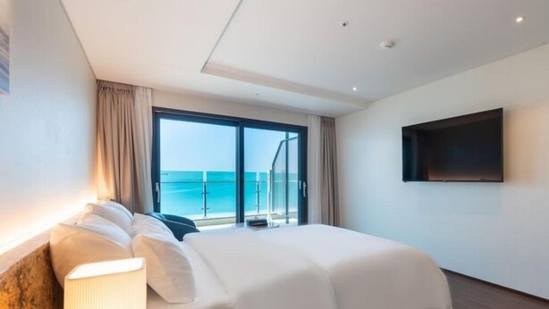 A hotel room with a bed, a TV, a balcony with a view of the sea, and a large window. - HOTEL GITE (Siheung)