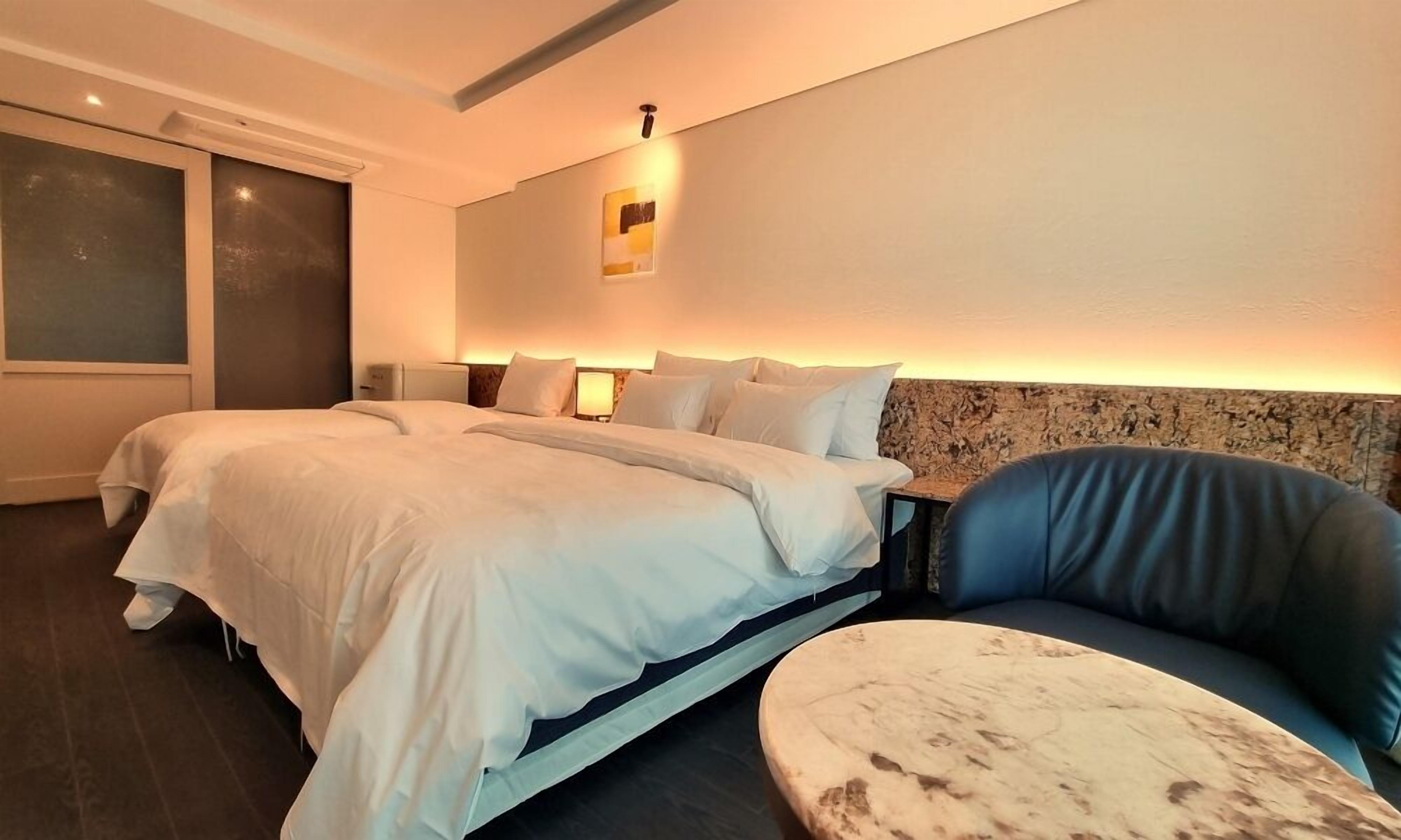 A modern hotel room with a large bed, a seating area with a round table, and a large window.