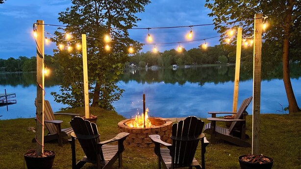 Et udendørs opholdsområde med Adirondack-stole, pejse og lyskæder.
