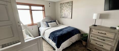 A bedroom with a bed, a dresser, a ceiling fan, a window, and a painting on the wall.