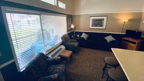 A compact living room with a sofa, a small table, a TV, and a window with blinds. - #168 Condo near large pool & shuttle to Gorge Amp-book separately (Quincy)