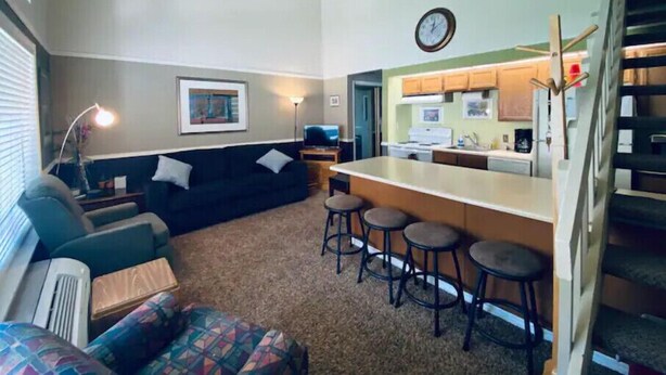 A compact living space with a sofa, a small coffee table, a bar area with stools, and a kitchenette in the background. - #168 Condo near large pool & shuttle to Gorge Amp-book separately (Quincy)