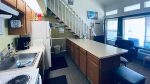 A compact kitchen with a refrigerator, stove, and sink. A staircase leads to a second level, and there are windows providing natural light. - #168 Condo near large pool & shuttle to Gorge Amp-book separately (Quincy)