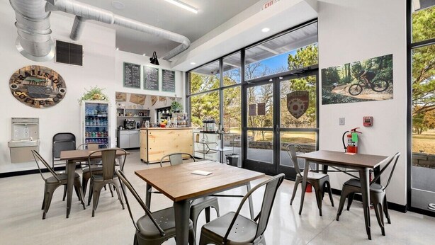 A modern cafe with tables and chairs, a coffee machine, and a menu board. - Long Shadow - MTB Oasis (Bella Vista)