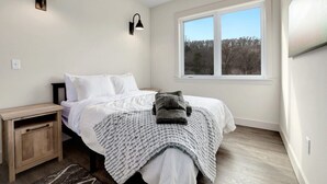 Une chambre à coucher comprenant un lit, des tables de chevet, une fenêtre et des luminaires fixés au mur.
