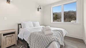 Ein Schlafzimmer mit Bett, Nachttischen, einem Fenster mit Blick und Wandleuchten.