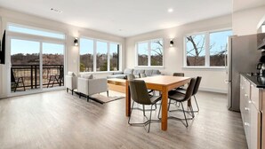 Een ruime woonkamer met een eettafel, stoelen, een bank en een keuken voorzien van een koelkast.