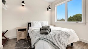 Een slaapkamer met een bed, twee wandlampen, een raam en een klein houten nachtkastje.