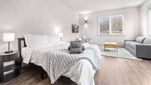 Quarto moderno com uma cama grande, um sofá, uma mesa pequena e uma janela com vista para árvores.