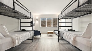 Une chambre de dortoir avec des lits superposés, un petit canapé, une table basse et une fenêtre donnant sur les arbres.