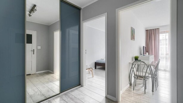 Een modern appartement met een schuiframen naar een balkon, een eethoek met metalen stoelen en een klein zithoekje met een bankje.