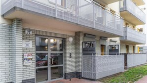 Een modern appartementencomplex met een glazen ingang, nummer 77, en een zichtbaar balkon.