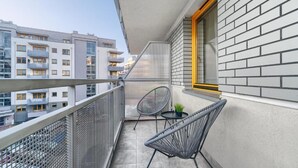 Een balkon met twee rieten stoelen, een klein tafeltje en een bloempot.