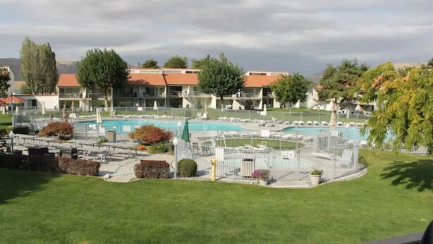 Uma área de piscina com várias piscinas, um gramado e edifícios com telhados vermelhos ao fundo.