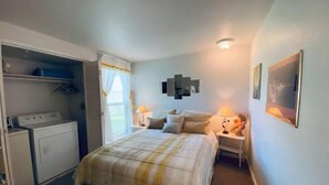 Quarto com cama, mesas de cabeceira, guarda-roupa e janela com cortinas.