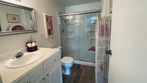 Casa de banho com lavatório branco, espelho e sanita. Existe cabine de duche com porta de vidro.