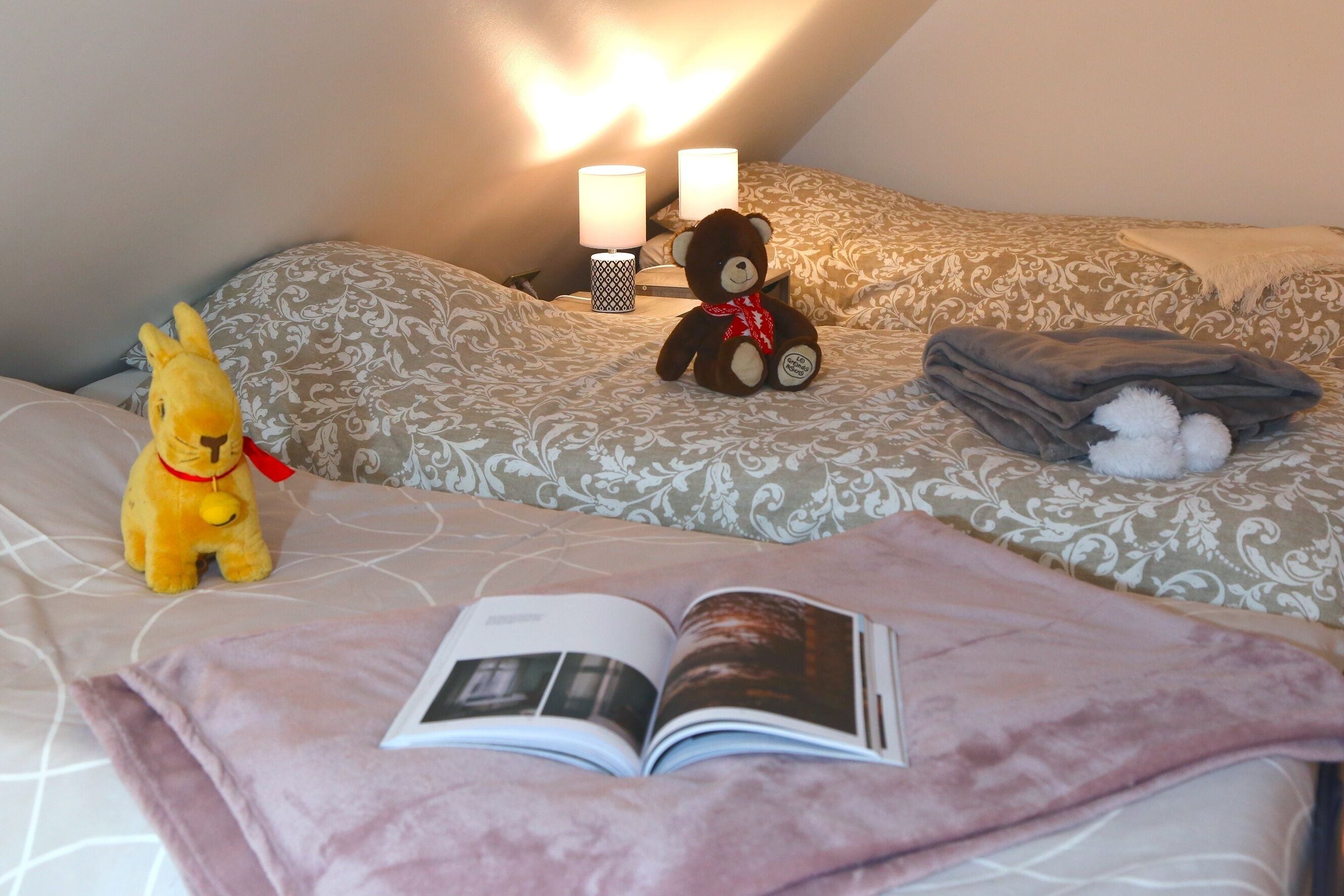 Una cama bien tendida con un libro, un osito de peluche y un juguete suave.