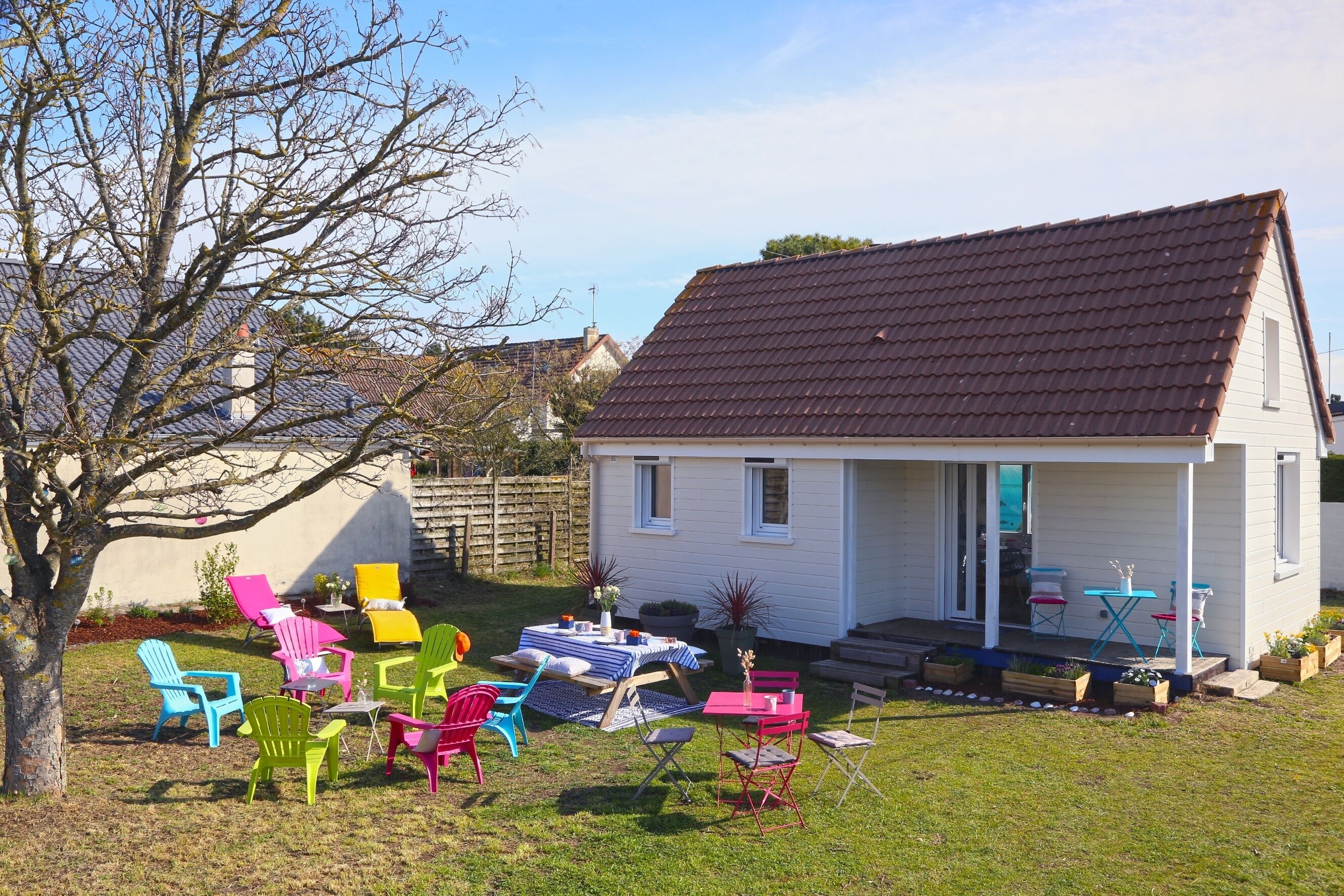 Ett hus med en veranda, färgglada stolar och ett bord dukat för måltider utomhus.