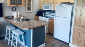 Une cuisine compacte dotée d’un îlot central, de meubles en bois, d’un four à micro-ondes et d’un réfrigérateur.