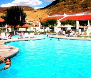Une piscine dotée de plusieurs couloirs, entourée de chaises longues et de parasols, avec en toile de fond un paysage montagneux.