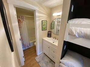 Cozy retreat with a single bed, bedside table, and bench, featuring a compact bathroom with a toilet and sink.