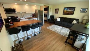 A modern kitchen with white cabinets, a wooden island with bar stools, a dining table with chairs, a black sofa, and a painting on the wall. - #181 Condo near large pool & shuttle to Gorge Amp-book separately (Quincy)