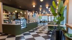 A cafe with a checkered floor, a green counter with a display case, and several tables and chairs. - Ring SPA Hostel (Tallinn)