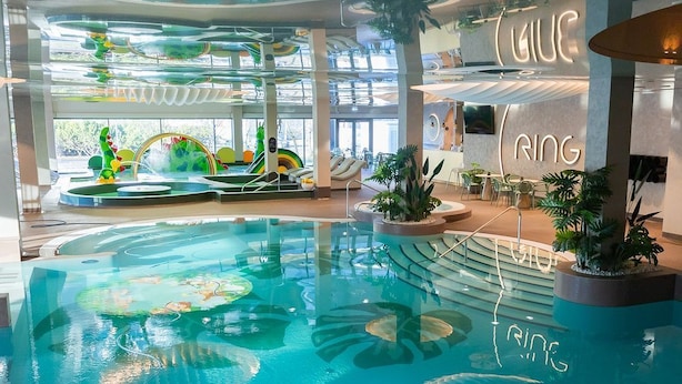 An indoor swimming pool with clear water, surrounded by seating areas and indoor plants. - Ring SPA Hostel (Tallinn)