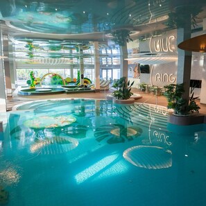Una piscina interior con agua cristalina, rodeada de zonas de estar y plantas de interior.