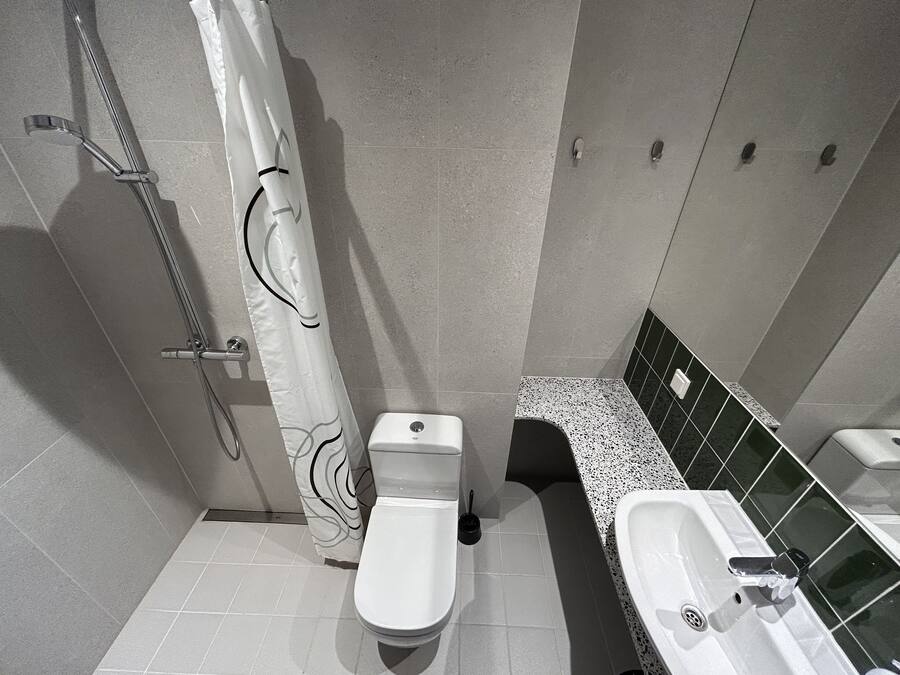 A bathroom with a toilet, a shower with a curtain, a sink, and a tiled floor.