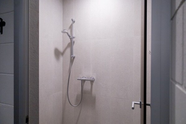 Ducha con cabezal de ducha de mano y grifo empotrado en una pared de baño con azulejos.