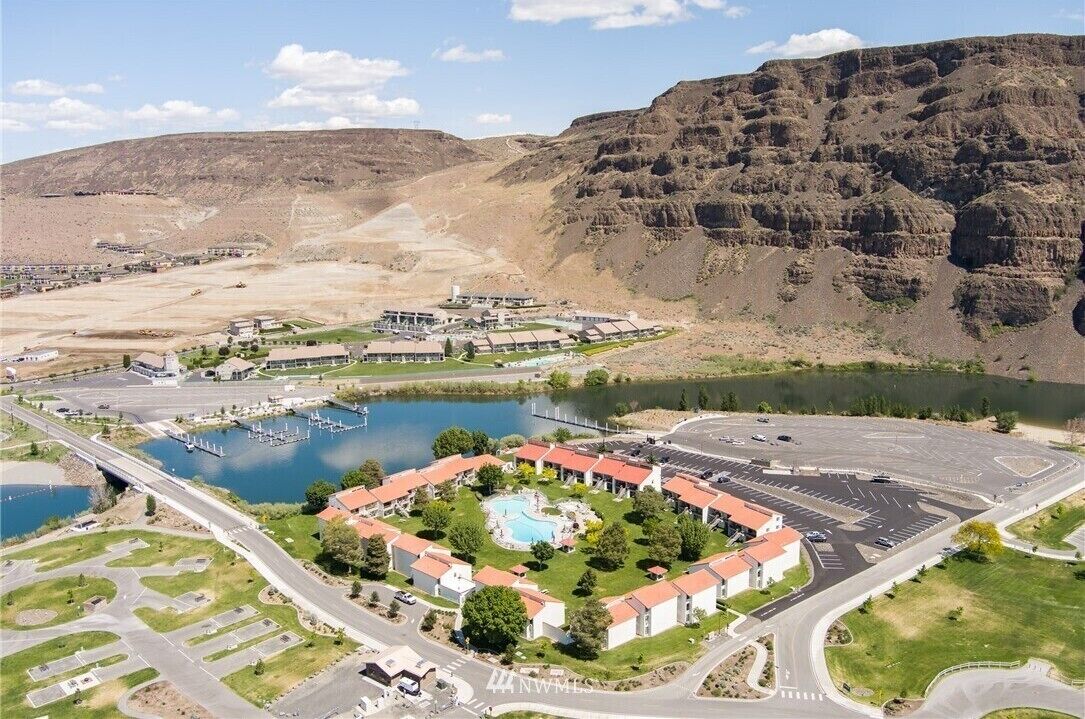 Vista aérea de un resort con piscina central, edificios conectados y un estacionamiento.