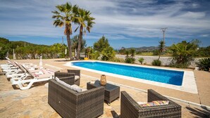 A poolside area with lounge chairs, wicker furniture, and a clear blue pool.