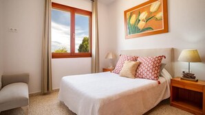 A bedroom with a bed, a chair, a nightstand, a lamp, a window, and a painting.
