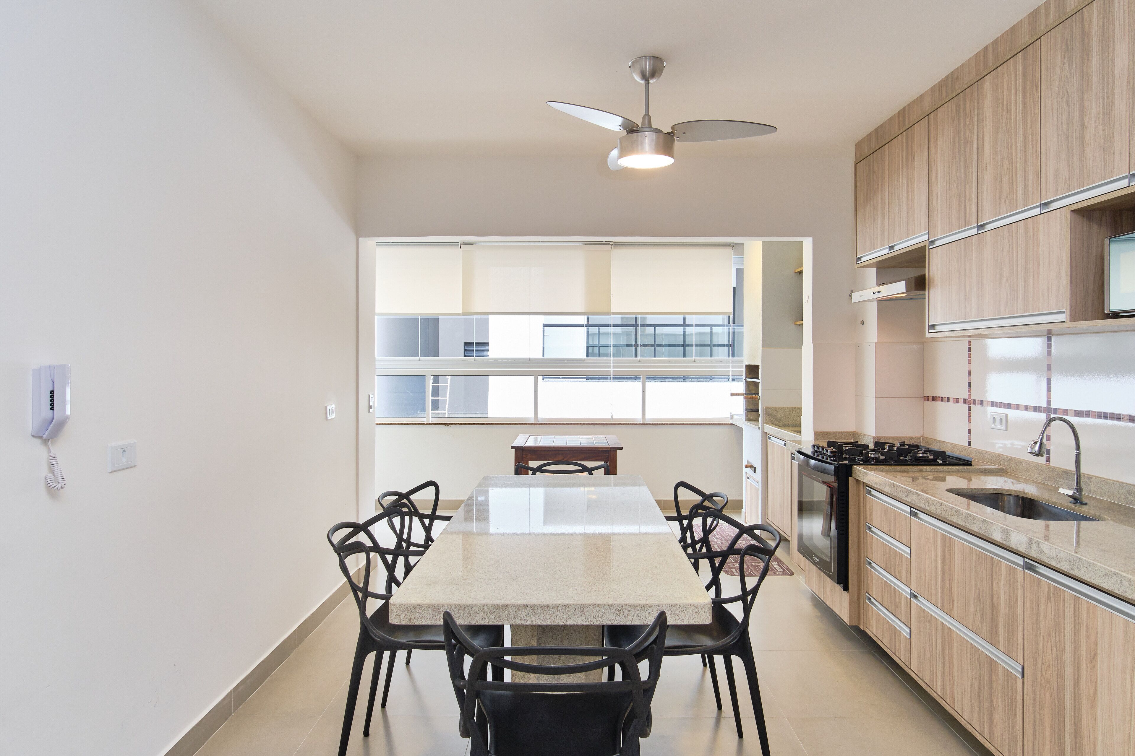 A modern kitchen with a dining table, chairs, a ceiling fan, and a view of the living area.