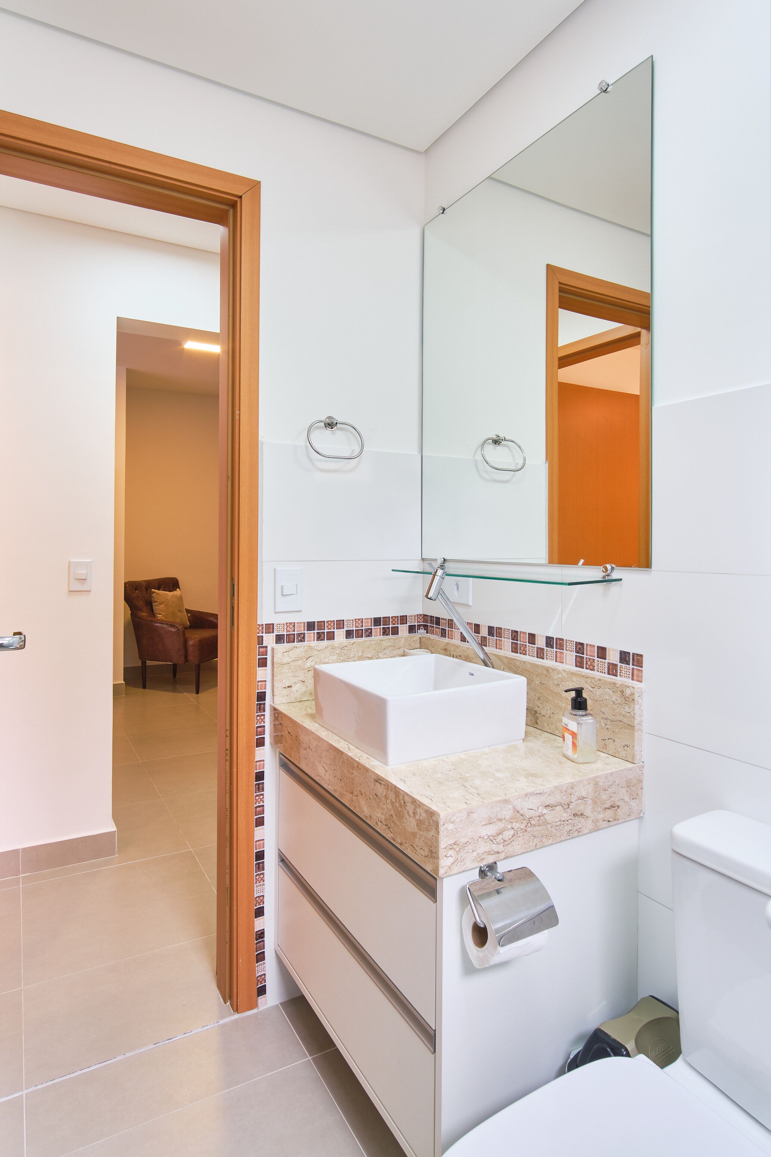 Une salle de bain moderne avec un lavabo blanc, une étagère en verre au-dessus du lavabo, des toilettes et un miroir.