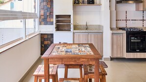 A modern kitchen with a dining area, featuring a stone accent wall, wooden cabinets, and a built-in oven. - Edífico Residencial Unique (Ubatuba)