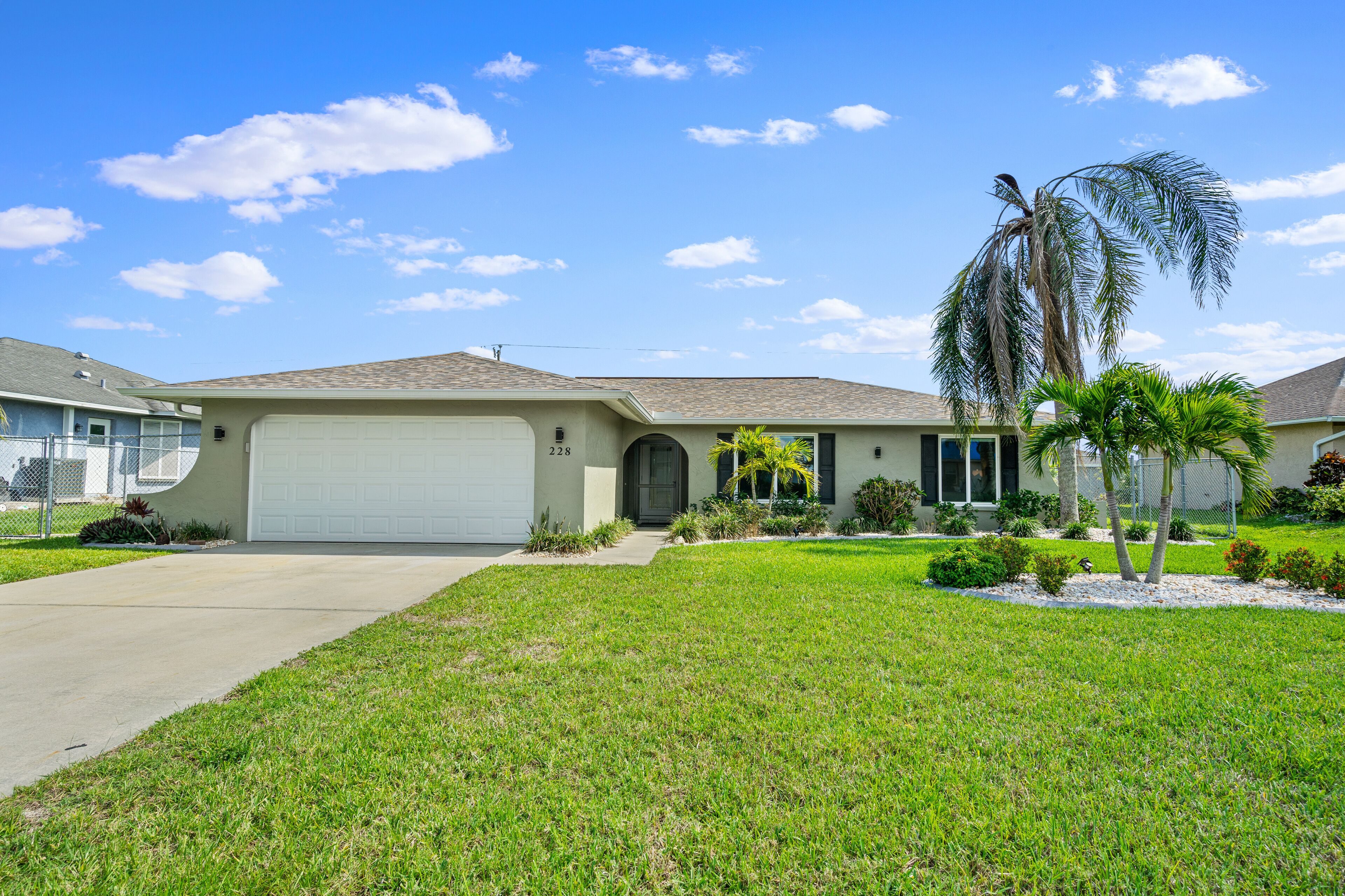 A single-story house with a garage, a well-maintained lawn, and two palm trees.