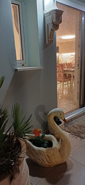 Una jardinera con forma de cisne adornada con flores, una ventana y una puerta con vistas a un espacio exterior.