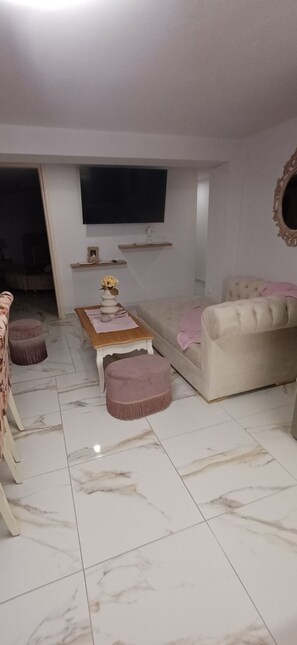 Un salon comprenant un canapé, des poufs, une table basse, un téléviseur fixé au mur et un miroir.