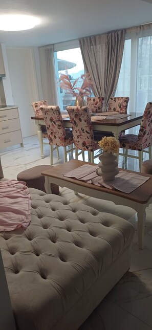 Un coin repas avec des chaises à motifs floraux, une table agrémentée d’un vase et un pouf capitonné.