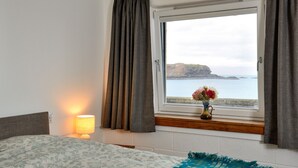 A bedroom with a bed, a bedside lamp, a window with curtains, and a vase with flowers. - Generals Yard (Eyemouth)